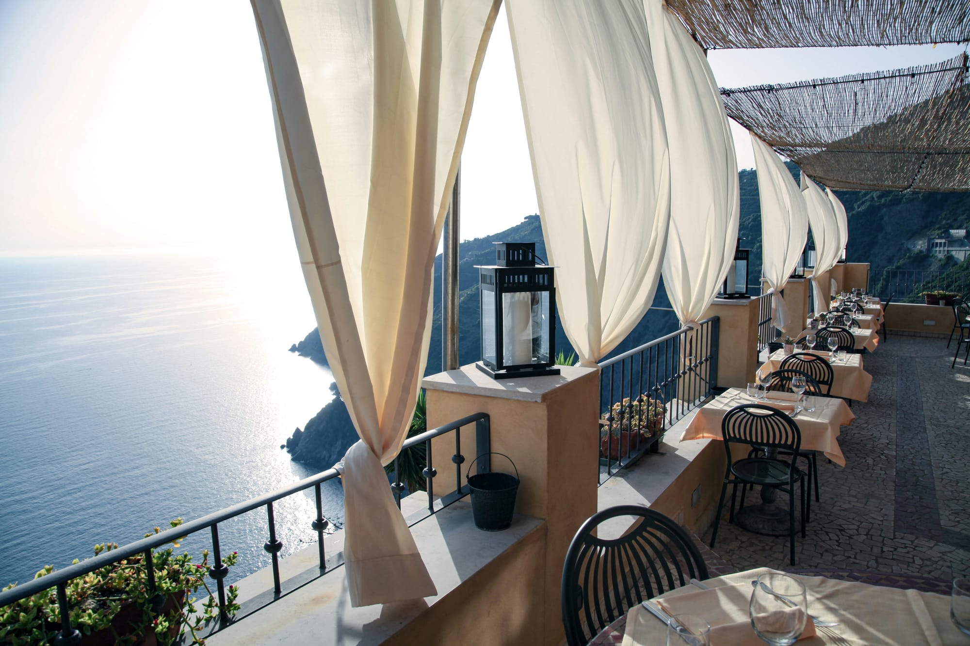 A quiet clifftop terrace with flowing white drapes overlooking the sea at golden hour