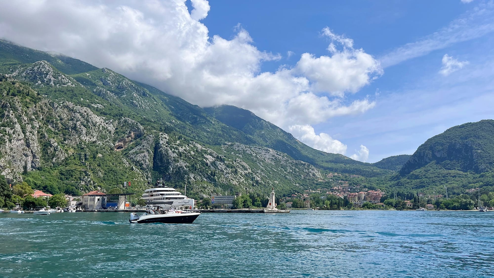 A boat on the turquoise water of the Bay of Kotor beneath green mountains